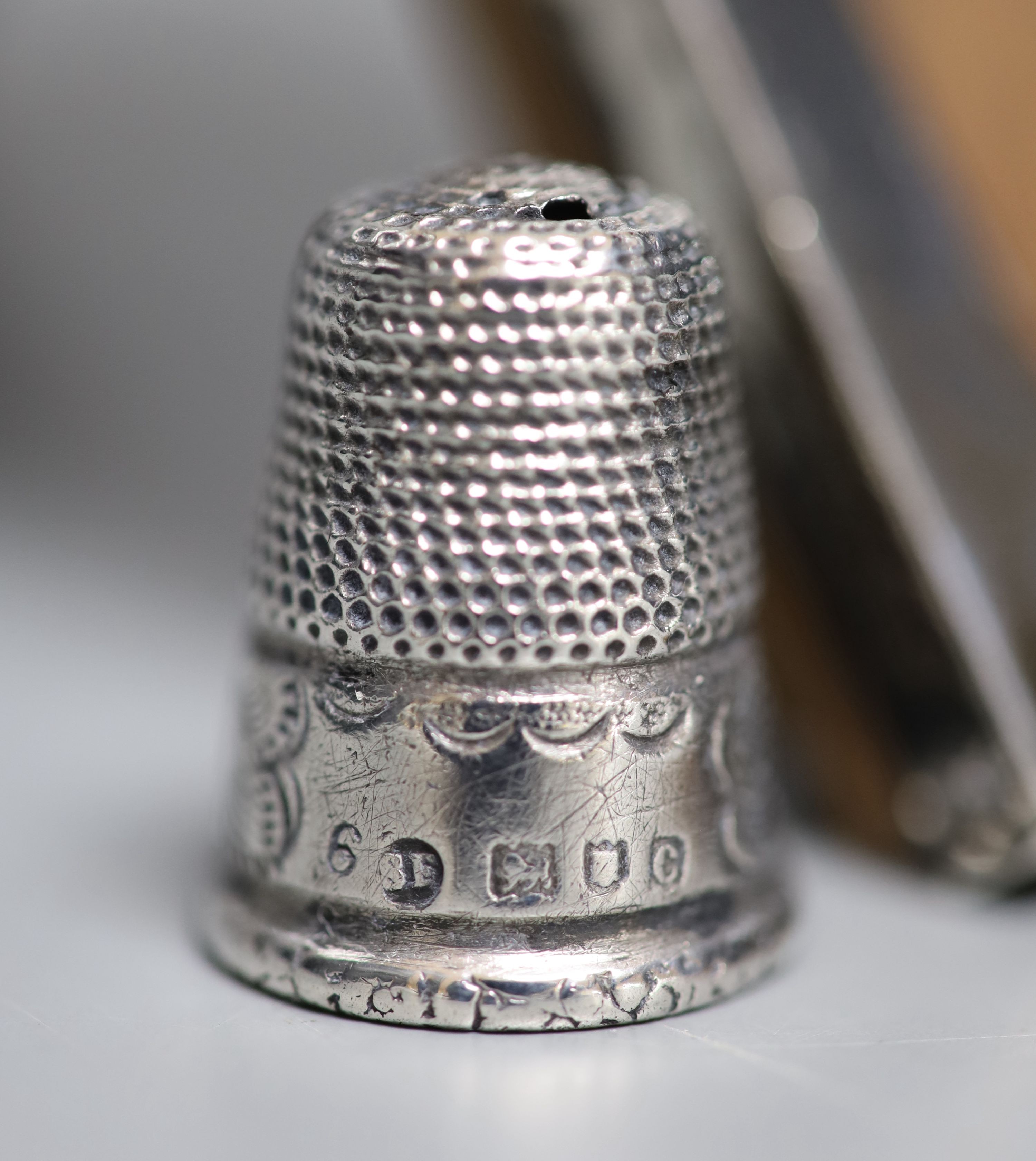 A silver mounted cigarette box, a silver mounted photograph frame, a silver thimble, a silver mounted comb(a.f.) and a silver mounted glass condiment bottle.